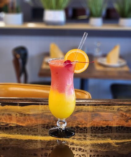 A layered orange and red drink with an orange slice and cherry